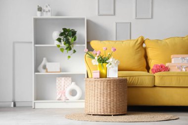 Anneler Günü için dekore edilmiş oturma odasının içinde sarı kanepe, sepet ve raf ünitesi var.