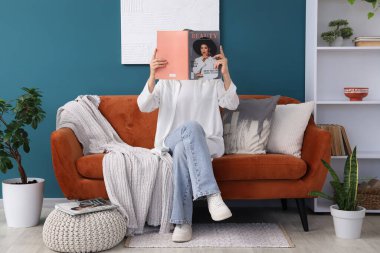 Evdeki kanepede dergi okuyan genç bir kadın.