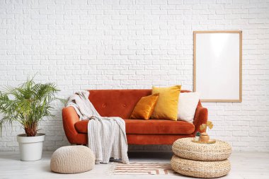 Rahat kahverengi kanepesi ve beyaz tuğla duvarın yanında pufları olan modern bir oturma odası.