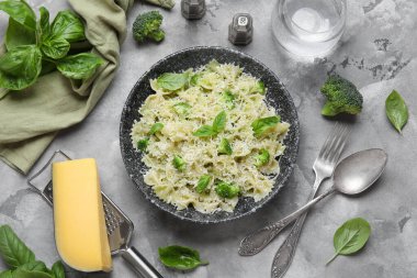 Gri arka planda fesleğen ve brokoli ile bir kase lezzetli farfalle makarna.