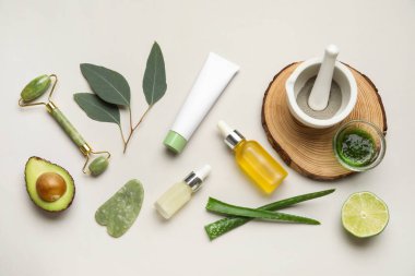 Kozmetik ürünleri şişeleri, yüz masajı aletleri ve beyaz arka plandaki malzemelerle kompozisyon