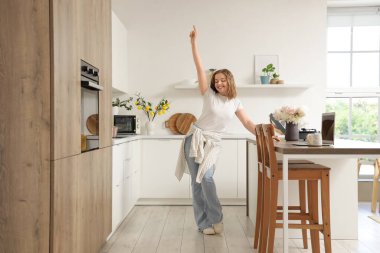 Güzel genç bayan mutfakta dans ediyor.