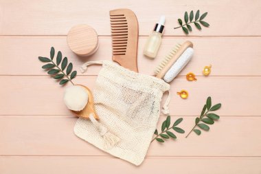 Çanta, saç fırçası, kapsüller, kavanoz ve pembe ahşap arka planda bulunan kozmetik ürünler.