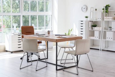 Konferans salonunun içinde masa, raf üniteleri ve bitkiler var.