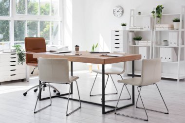 Konferans salonunun içinde masa, raf üniteleri ve bitkiler var.