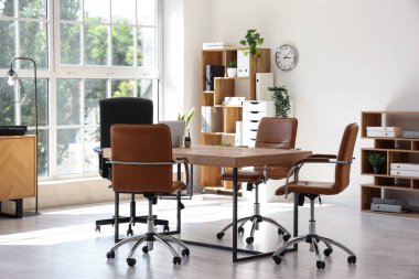 Konferans salonunun içinde masa, raf üniteleri ve bitkiler var.