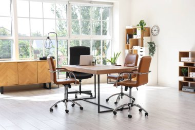 Konferans salonunun içinde masa, raf üniteleri ve bitkiler var.