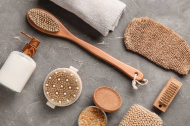 Gri grunge arka planda masaj vücut fırçaları, havlu ve bir şişe kozmetik ürünü ile kompozisyon, yakın plan.