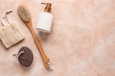 Masaj fırçası, sünger taşı ve pembe grunge arka planda bir şişe kozmetik ürünü, yakın plan.