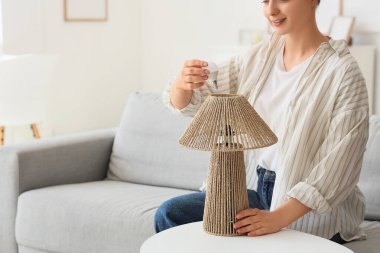 Genç bir kadın evdeki masada ampulü lambaya vidaladı.