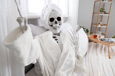 Havlu ve bornozlu insan iskelet modeli yatak odasında selfie çekiyor.