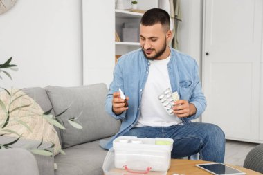 Genç adam evde ilk yardım çantasından ilaç ve damla alıyor.