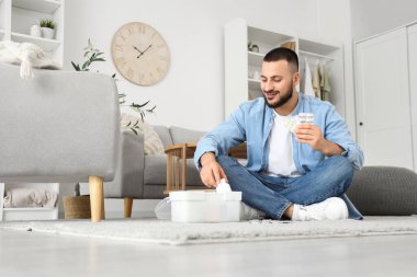 Genç adam evdeki ilk yardım çantasından hap alıyor.