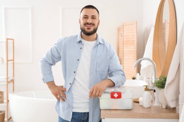 Banyoda ilk yardım çantası olan genç bir adam var.