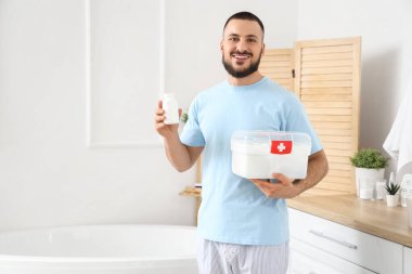 Banyoda ilk yardım çantası ve ilaç şişesi olan genç bir adam.