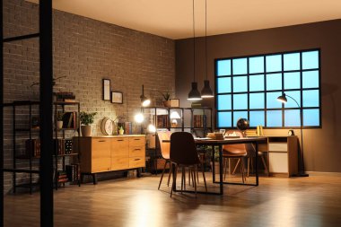 Geceleri kitap rafları, masalar ve parlayan lambalarla dolu karanlık bir oda.