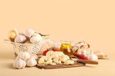 Kolander ve ahşap tahta. Bej arka planda farklı sebzelerle taze sarımsak.