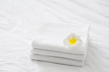 Otel odasındaki yatağın üzerinde beyaz Plumeria çiçeği olan bir yığın temiz havlu.