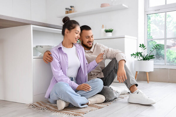 Молодая пара с ключом от своей новой квартиры, сидящей на полу на кухне