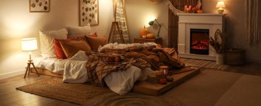 Şık yatak odasının içinde sonbahar süslemeleri ve şöminede mumlar var.