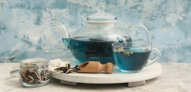 Kelebek çiçekli çay fincanı ve mavi grunge arka planda ahşap tepsi.