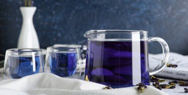 Çaydanlık ve bir fincan kelebek bezelye çiçeği çayı mavi arka planda.