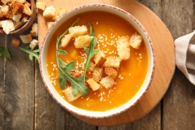 Tahta zemin üzerinde kızarmış ekmek ve roka olan lezzetli balkabağı kremalı çorba.