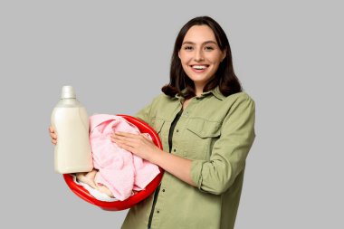 Çamaşır sepeti ve gri arka planda bir şişe deterjanı olan genç bir kadın.