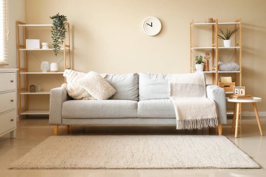 Beyaz duvarın yanında kanepesi, masası ve ahşap rafları olan modern oturma odasının içinde.