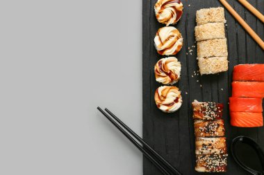 Lezzetli suşi ruloları, yemek çubukları ve gri arka planda kaşık olan tahta.