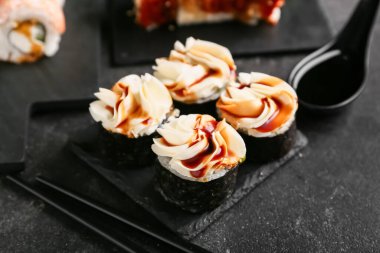 Lezzetli suşi ruloları ve siyah grunge arka planda çubukları olan tahta, yakın plan.