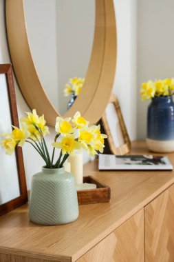Çekmeceler, aynalar ve vazolar. Odada narsist çiçekler var.