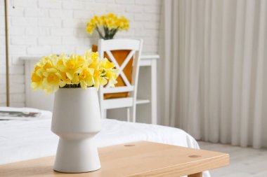 Sarı narsist çiçekli vazo beyaz yatak odasının yanındaki bankta.