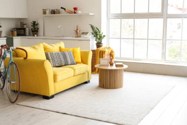 İçinde sarı kanepe, sehpa, tezgah ve bisiklet olan oturma odası.