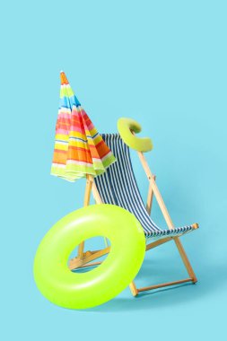 Renkli şemsiyeli çizgili güverte sandalyesi ve mavi arka planda şişme yüzük.