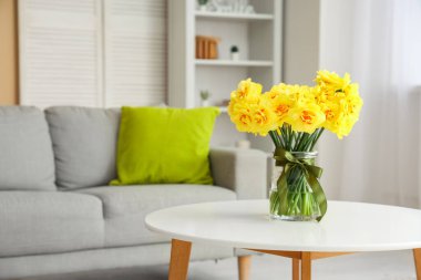 Oturma odasındaki vazoda yastıklı ve nergis çiçekli rahat kanepe.