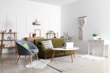 Oturma odasında rahat bir kanepe, koltuk, raf ünitesi ve zeytin ağacı var.