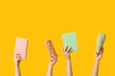 Sarı zemin üzerinde kalem kılıfları ve defterleri olan kadın eller.