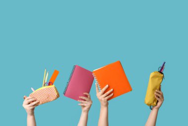 Mavi arka planda kırtasiyeli defter ve kalem kılıfları tutan kadın eller.