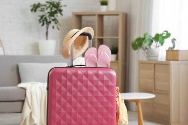 Oturma odasında şapka ve parmak arası terliklerle dolu bavul.