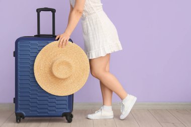 Leylak arka planda bavulu ve şapkası olan genç bir kadın.