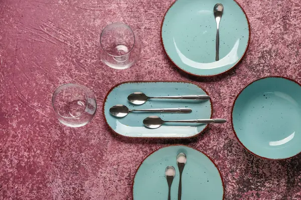 Temiz tabaklar, bardaklar ve koyu pembe masadaki çatal bıçak takımı.