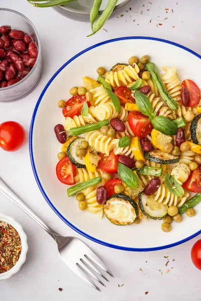 Bir kase domatesli makarna salatası ve beyaz arka planda fesleğen.