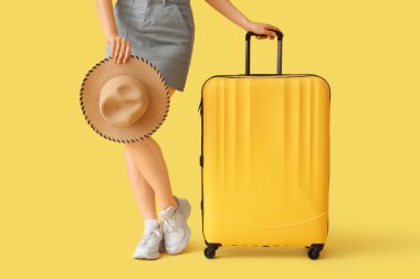 Sarı arka planda bavulu ve şapkası olan genç bir kadın.