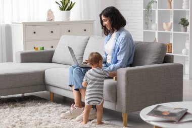 Sevimli bebek ve evde doğum izninde dizüstü bilgisayarla çalışan mutlu genç anne.