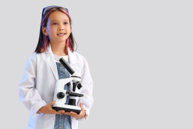 Gri arka planda mikroskobu olan sevimli küçük bir kız.
