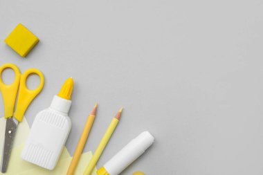 Bir şişe tutkal, yapıştırıcı, makas ve gri arka planda kalemler. Üst görünüm