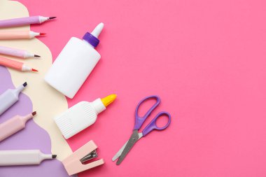 Bir şişe tutkal, keçeli kalemler ve pembe arka planda keçeli kalemler. Üst görünüm