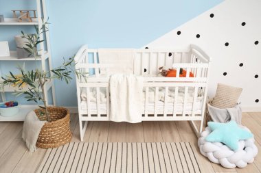 Çocukların odasının içindeki mavi duvarın yanında ekose ve raf üniteli şık beyaz bir beşik.