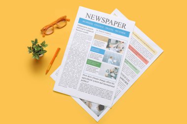 Gazete, gözlük, ev bitkisi ve sarı arka planda kalem. Üst görünüm